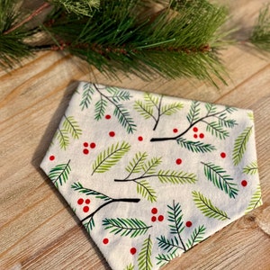 May include: A white fabric bandana with a green and red holiday print of pine branches and berries.