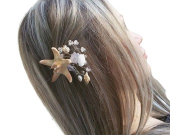 May include: A hair clip featuring a starfish, seashells, and white flowers with crystal accents. The clip is made of metal and has a gold finish.