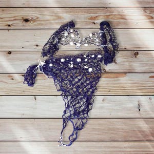 May include: A blue and white crocheted net with white beads. The net is laid out on a wooden surface.