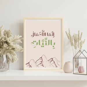 Könnte beinhalten: Ein gerahmter Druck mit einem hellrosa Hintergrund, der eine Bergkette und arabischen Text in Grün und Braun zeigt, der "إنما الله معمال بالنيّات" lautet.