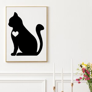 May include: Black and white silhouette of a cat with a heart on its chest. The cat is sitting with its tail curled around its body. The image is framed in a gold frame.