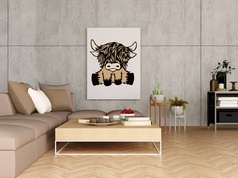 May include: A white canvas print with a cartoon illustration of a brown and black Highland cow sitting with its legs crossed. The print is hanging on a gray concrete wall in a living room setting.