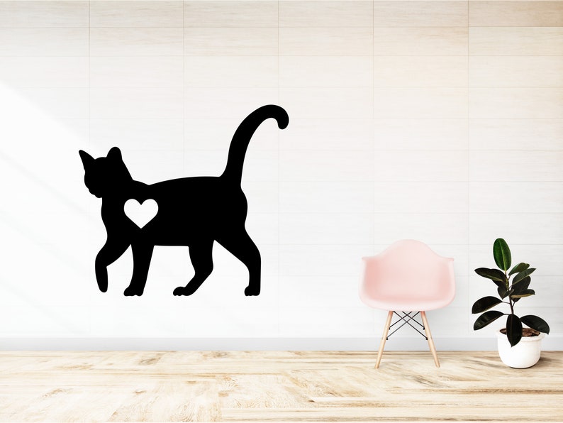 May include: A black silhouette of a cat with a white heart on its chest. The cat is walking to the right. The image is on a white wall with a pink chair and a potted plant in the background.