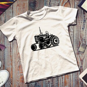 Op de afbeelding: Een wit T-shirt met een zwart silhouet van een vintage tractor. De tractor heeft grote wielen en een gedetailleerd ontwerp.