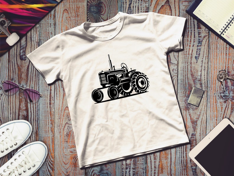Op de afbeelding: Een wit T-shirt met een zwart silhouet van een vintage tractor. De tractor heeft grote wielen en een gedetailleerd ontwerp.