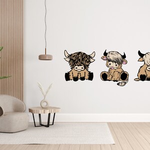 May include: Three cartoon Highland cow illustrations in a row on a white wall. The cows are brown and white with black eyes and noses. They are sitting with their legs tucked under them and their tails curled up.