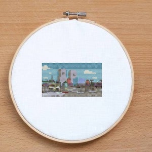 May include: A cross-stitch pattern featuring a colorful cityscape with buildings, trees, and a blue sky.