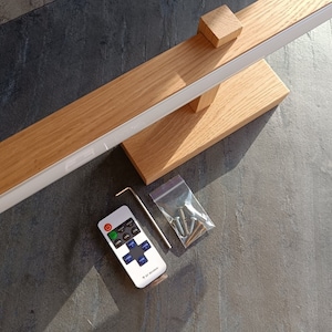 May include: A wooden wall-mounted light fixture with a white LED strip and a remote control. The remote has buttons for power, brightness, and color temperature. The light fixture comes with screws and a hex wrench for installation.
