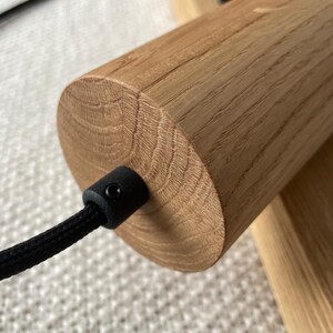 Op de afbeelding: Close-up van een houten onderdeel van een lamp. Het cilindrische houten stuk heeft een natuurlijke houtnerf en een zwart snoer dat eruit komt. De armatuur is gemonteerd op een houten basis, wat wijst op een modern ontwerp.