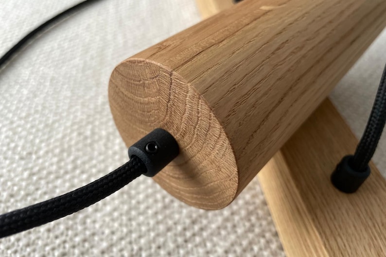 Op de afbeelding: Close-up van een houten onderdeel van een lamp. Het cilindrische houten stuk heeft een natuurlijke houtnerf en een zwart snoer dat eruit komt. De armatuur is gemonteerd op een houten basis, wat wijst op een modern ontwerp.