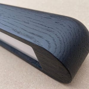 Puede incluir: Primer plano de un objeto de madera negra con un extremo redondeado y una secci&oacute;n blanca empotrada. La veta de la madera es visible y el acabado es mate. El objeto parece ser una pieza decorativa o funcional.