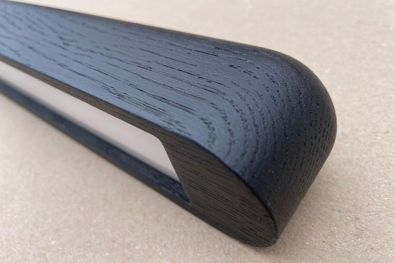 Puede incluir: Primer plano de un objeto de madera negra con un extremo redondeado y una secci&oacute;n blanca empotrada. La veta de la madera es visible y el acabado es mate. El objeto parece ser una pieza decorativa o funcional.