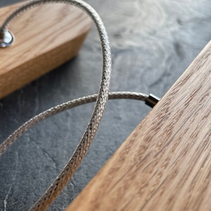 Close-up of a natural oak wood pendant light showing the fine grain and texture of the wood, with a strong and elegant steel cable suspension used for mounting and powering the fixture. Ideal for modern and minimalist interiors.