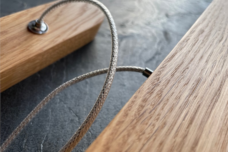 Close-up of a natural oak wood pendant light showing the fine grain and texture of the wood, with a strong and elegant steel cable suspension used for mounting and powering the fixture. Ideal for modern and minimalist interiors.