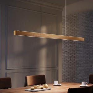 May include: A long, rectangular wooden pendant light fitting suspended above a dining table. The light has a warm, natural wood finish and a bright, linear light source. The dining room features a dark wood table, brown chairs, and a grey wall.