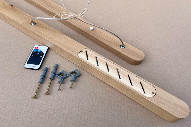 Puede incluir: Una l&aacute;mpara lineal de madera clara con un panel central de listones diagonales, un cable de suspensi&oacute;n plateado, un peque&ntilde;o mando a distancia con botones y cuatro tornillos met&aacute;licos con tacos de pl&aacute;stico para su instalaci&oacute;n.