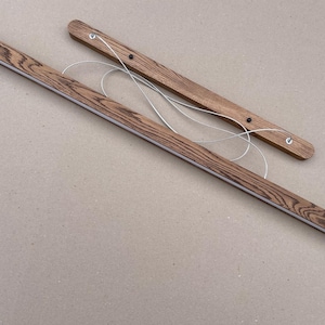 Puede incluir: Dos barras de madera rectangulares y largas para colgar p&oacute;steres con un prominente patr&oacute;n de veta de madera marr&oacute;n oscuro. Cada barra incluye un hilo met&aacute;lico fino de color plateado unido a la parte superior para colgar.