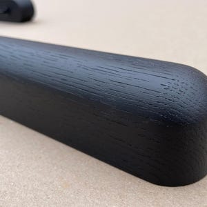 Puede incluir: Primer plano de una percha de madera negra con un extremo redondeado. La veta de la madera es visible y la percha parece lisa y bien acabada. La percha est&aacute; dise&ntilde;ada para ropa.
