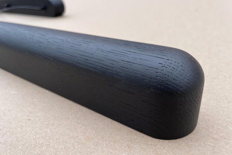 Puede incluir: Primer plano de una percha de madera negra con un extremo redondeado. La veta de la madera es visible y la percha parece lisa y bien acabada. La percha est&aacute; dise&ntilde;ada para ropa.