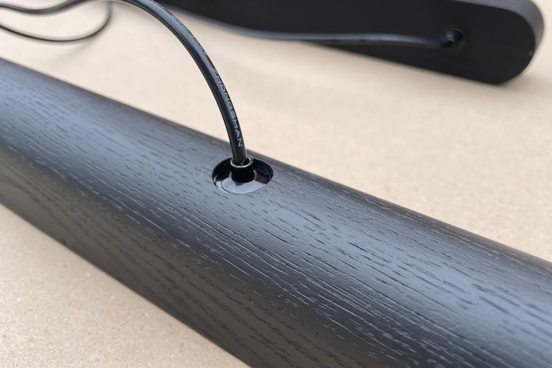 Puede incluir: Primer plano de un componente de madera negro para una l&aacute;mpara con un agujero para un cable. La veta de la madera es visible. Un cable negro est&aacute; insertado en el agujero. Otro componente similar est&aacute; en el fondo.