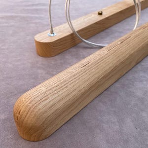 Puede incluir: Primer plano de dos l&aacute;mparas de madera. Las l&aacute;mparas est&aacute;n hechas de madera de color claro con extremos redondeados. Cada l&aacute;mpara tiene un cable met&aacute;lico para colgar. El fondo es una tela gris claro.