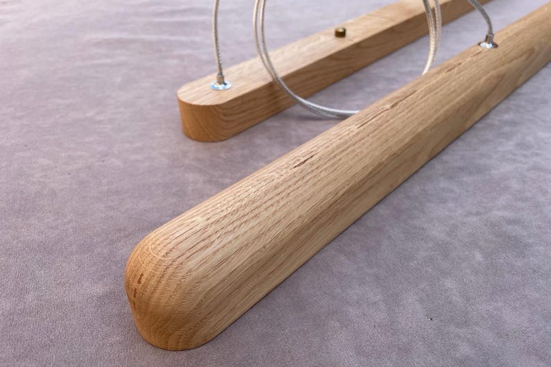 Puede incluir: Primer plano de dos l&aacute;mparas de madera. Las l&aacute;mparas est&aacute;n hechas de madera de color claro con extremos redondeados. Cada l&aacute;mpara tiene un cable met&aacute;lico para colgar. El fondo es una tela gris claro.