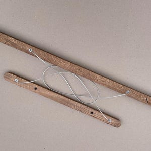 Puede incluir: Dos listones de madera alargados de color marr&oacute;n medio con una textura de veta visible. Los listones est&aacute;n conectados por un alambre met&aacute;lico fino de color plateado que forma un bucle entre ellos. Un list&oacute;n tiene ranuras diagonales.