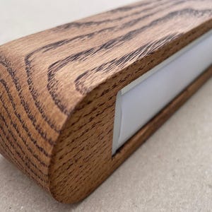 Puede incluir: Una luminaria lineal con una carcasa de madera marr&oacute;n natural con un patr&oacute;n de veta prominente y un extremo redondeado. La luminaria incluye una tira difusora blanca larga y empotrada a lo largo de su longitud para emitir luz de forma uniforme.