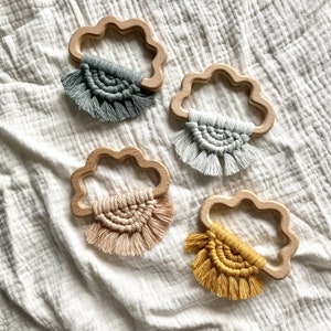 Può includere: Quattro giocattoli da dentizione in legno a forma di nuvola con frange all'uncinetto di diversi colori. Le frange sono in tonalità di grigio, beige, rosa e giallo.