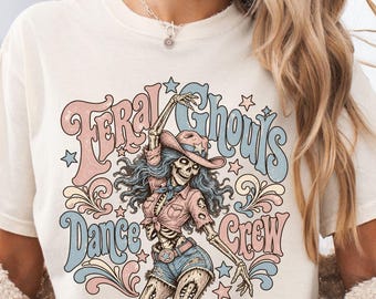 Könnte beinhalten: Ein elfenbeinfarbenes T-Shirt mit einem Grafikdruck eines Skeletts, das einen Cowboyhut, ein Hemd mit Kragen und Jeansshorts trägt. Der Text "Feral Ghouls Dance Crew" ist in einer Retro-Schrift um das Skelett herum gedruckt, verziert mit Sternen.