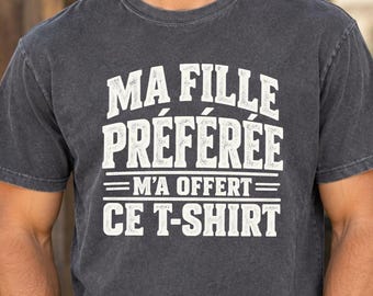Könnte beinhalten: Ein anthrazitfarbenes Kurzarm-T-Shirt mit Rundhalsausschnitt. Auf der Vorderseite befindet sich ein weißer Schriftzug im Used-Look mit dem Text: MA FILLE PRÉFÉRÉE M'A OFFERT CE T-SHIRT. Das Kleidungsstück hat eine lockere Passform.