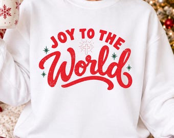 Könnte beinhalten: Ein weißes Sweatshirt mit Rundhalsausschnitt und dem roten Schriftzug Joy To The World sowie einem kleinen weißen Kreuzsymbol in der Mitte. Das Design enthält kleine grüne Sternakzente. Das Sweatshirt wird mit einer rot-schwarz karierten Schlafhose kombiniert.