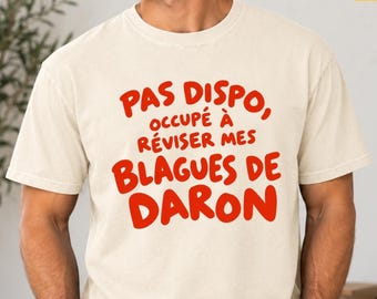 Könnte beinhalten: Ein elfenbeinfarbenes Kurzarm-T-Shirt mit rotem Textaufdruck auf der Vorderseite: PAS DISPO, OCCUPÉ À RÉVISER MES BLAGUES DE DARON. Das Kleidungsstück hat einen Rundhalsausschnitt und eine Standardpassform aus einfarbigem Stoff.