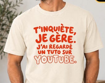 Könnte beinhalten: Ein elfenbeinfarbenes Kurzarm-T-Shirt mit rotem Textaufdruck: T'INQUIÈTE, JE GÈRE. J'AI REGARDÉ UN TUTO SUR YOUTUBE. Das Shirt hat einen Rundhalsausschnitt und eine lockere Passform mit kräftigen, zentrierten Buchstaben auf der Brust.
