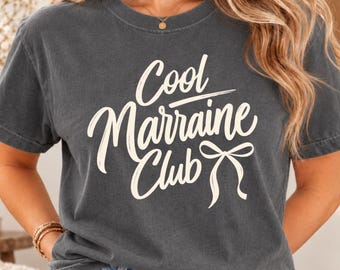Könnte beinhalten: Ein anthrazitfarbenes Kurzarm-T-Shirt mit dem weißen Schriftzug Cool Marraine Club und einer kleinen Schleifengrafik. Das Shirt hat einen Rundhalsausschnitt und eine lockere Passform aus einfarbigem Stoff mit leicht verwaschener Optik.
