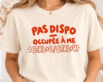 Könnte beinhalten: Ein elfenbeinfarbenes T-Shirt mit kurzen Ärmeln und rotem Text, der PAS DISPO OCCUPÉE À ME CTRL+C / CTRL+V lautet. Das Shirt hat einen Rundhalsausschnitt und wird mit einer blauen Jeans getragen. Das Design ist mittig auf der Brust platziert.