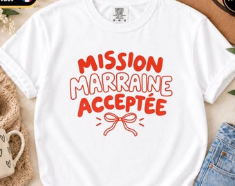Könnte beinhalten: Ein weißes T-Shirt mit kurzen Ärmeln und dem roten Schriftzug MISSION MARRAINE ACCEPTÉE in einer fetten, abgerundeten Schriftart, mittig auf der Brust platziert, mit einer kleinen roten Liniengrafik einer Schleife darunter.