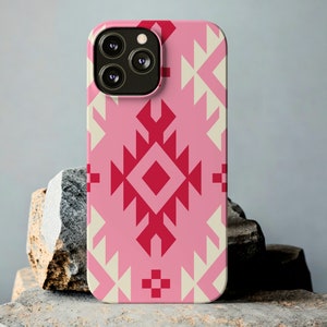 Puede incluir: Una funda de teléfono rosa con un patrón geométrico en tonos rosa y blanco roto. La funda tiene un recorte para la cámara y se muestra sobre una superficie texturizada.