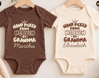 Könnte beinhalten: Zwei kurzärmelige Babybodys, einer in Braun und einer in Naturcreme, jeweils mit dem Text "Hand picked from heaven by grandma" und einem Heiligenschein-Motiv. Der braune Body ist mit "Martha" und der cremefarbene mit "Elizabeth" personalisiert.