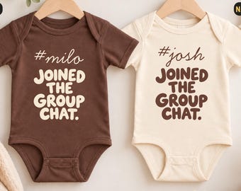 Könnte beinhalten: Zwei kurzärmelige Babybodys an Holzkleiderbügeln. Der braune Body trägt den weißen Schriftzug #milo JOINED THE GROUP CHAT. Der naturfarbene Body trägt den braunen Schriftzug #josh JOINED THE GROUP CHAT.