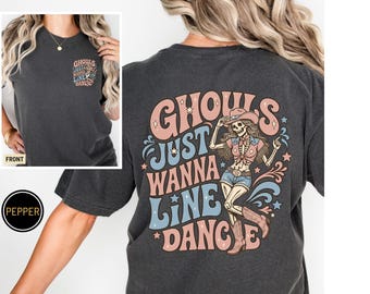 Könnte beinhalten: Ein anthrazitfarbenes T-Shirt mit einem Motiv auf der Rückseite und einer kleineren Version auf der linken Brust. Das Design zeigt ein Skelett mit Cowboyhut, Stiefeln und Fransenweste sowie den Schriftzug GHOULS JUST WANNA LINE DANCE in Rosa und Blau.