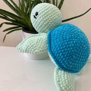 May include: A crocheted sea turtle toy with a light green body and blue shell. The toy has black eyes and a small smile.