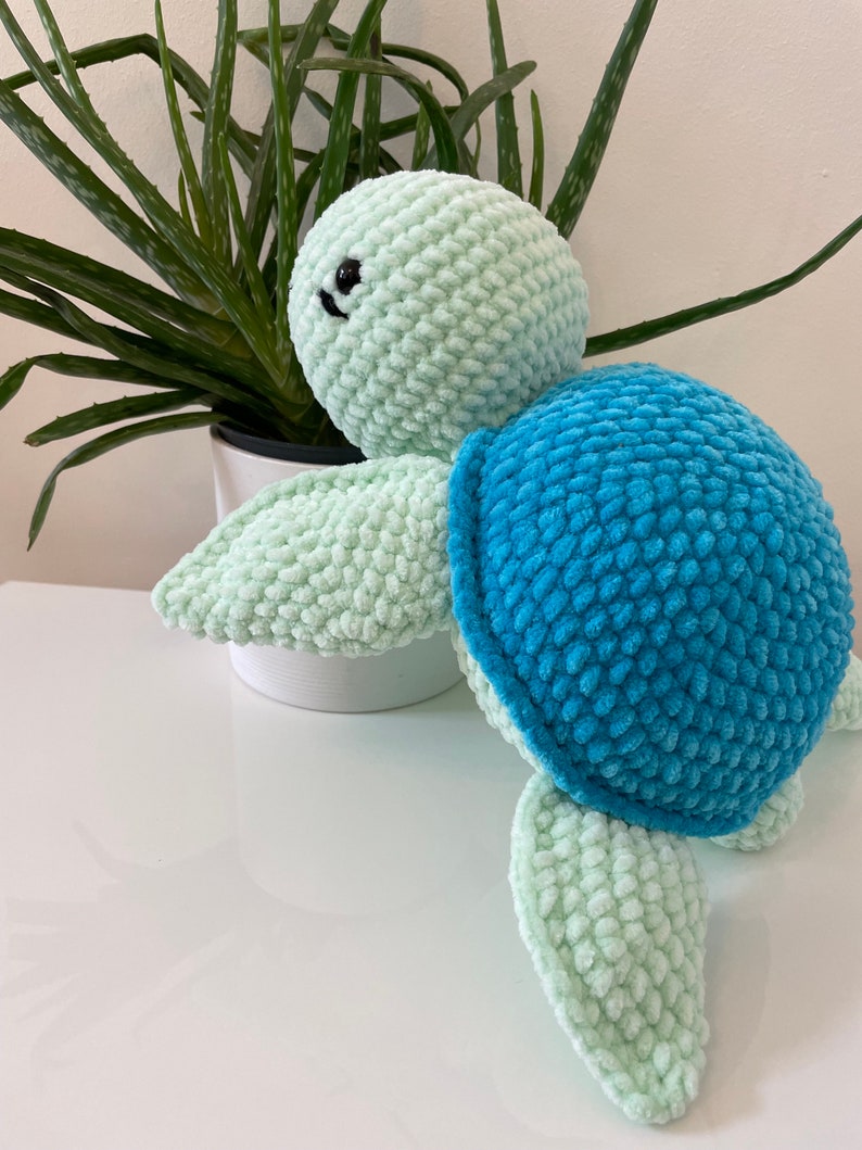 May include: A crocheted sea turtle toy with a light green body and blue shell. The toy has black eyes and a small smile.