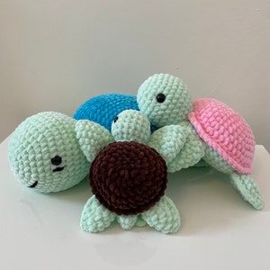 May include: Three crocheted turtle plush toys. One is light green, one is light blue, and one is pink. The turtles are stacked on top of each other.