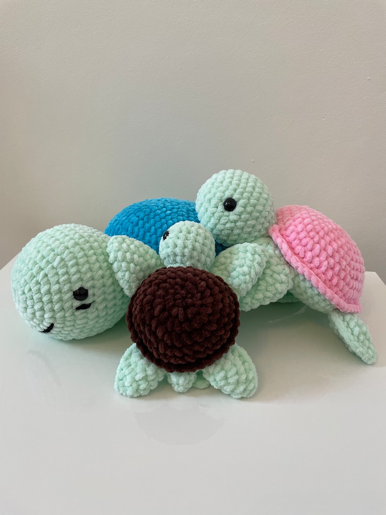 May include: Three crocheted turtle plush toys. One is light green, one is light blue, and one is pink. The turtles are stacked on top of each other.