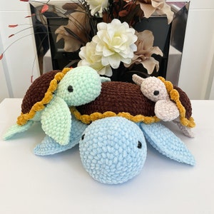 May include: Three crocheted turtle toys. One is light blue, one is brown with a yellow trim, and one is light green. The turtles are stacked on top of each other.