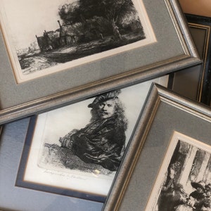 May include: A collection of framed black and white etchings. The artwork includes a landscape with a tree and buildings, a portrait of a man, and a scene with multiple figures. The frames are silver and gray.