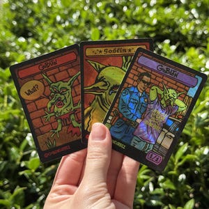 May include: Three rectangular trading cards with holographic finishes featuring goblin illustrations. The cards display the text "Goblin", "What?", and "I paused my game to be here" alongside a police officer figure. Each card has a black border.