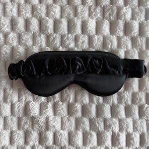 Pu&ograve; includere: Una mascherina per dormire di colore nero tinta unita, caratterizzata da una copertura oculare liscia e sagomata e da un cinturino elastico nero abbinato con una texture in tessuto arricciato e increspato. Il design &egrave; uniforme nel colore.