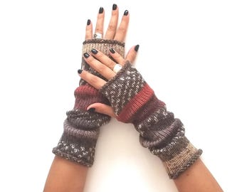 May include: A pair of fingerless gloves featuring a multi-colored knit pattern in shades of brown, tan, and muted red. The gloves have a ribbed texture with horizontal stripes and a small white speckled design throughout the fabric.